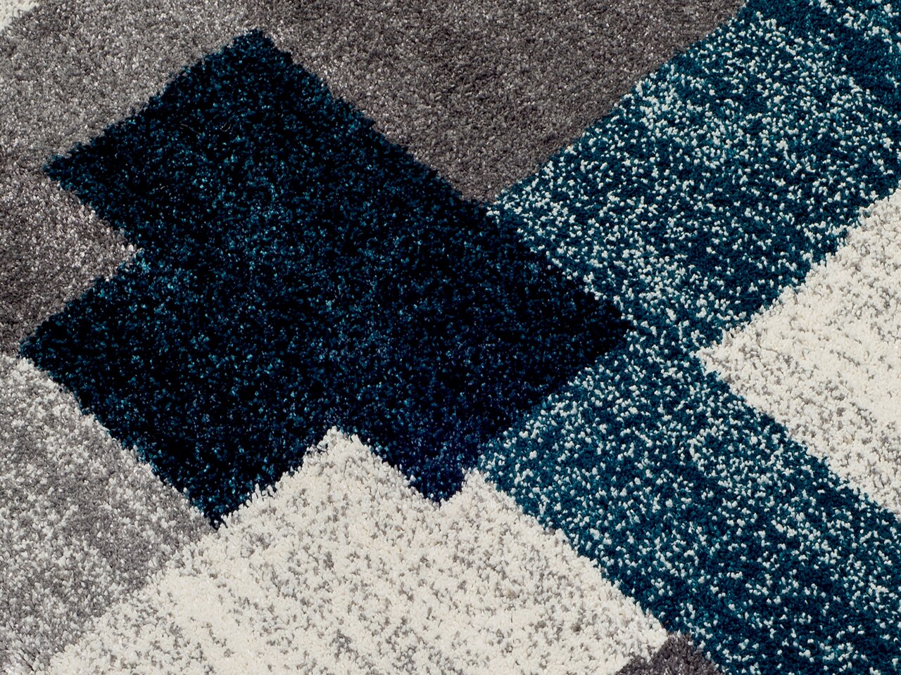 Nahaufnahme eines Frisé-Teppichs mit geometrischem Muster in Grau, Blau und Weiß.