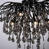 Nahaufnahme einer modernen Deckenleuchte mit vielen hängenden, tropfenförmigen Glaselementen und leuchtenden Glühbirnen, von unten betrachtet.