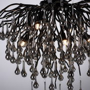 Nahaufnahme einer modernen Deckenleuchte mit vielen hängenden, tropfenförmigen Glaselementen und leuchtenden Glühbirnen, von unten betrachtet.