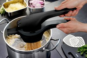 Kartoffel- und Spätzlepresse in der Seitenansicht, die über einem Topf gehalten wird, während Spätzle in kochendes Wasser gepresst werden.