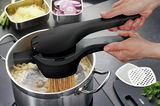 Kartoffel- und Spätzlepresse in der Seitenansicht, die über einem Topf gehalten wird, während Spätzle in kochendes Wasser gepresst werden.