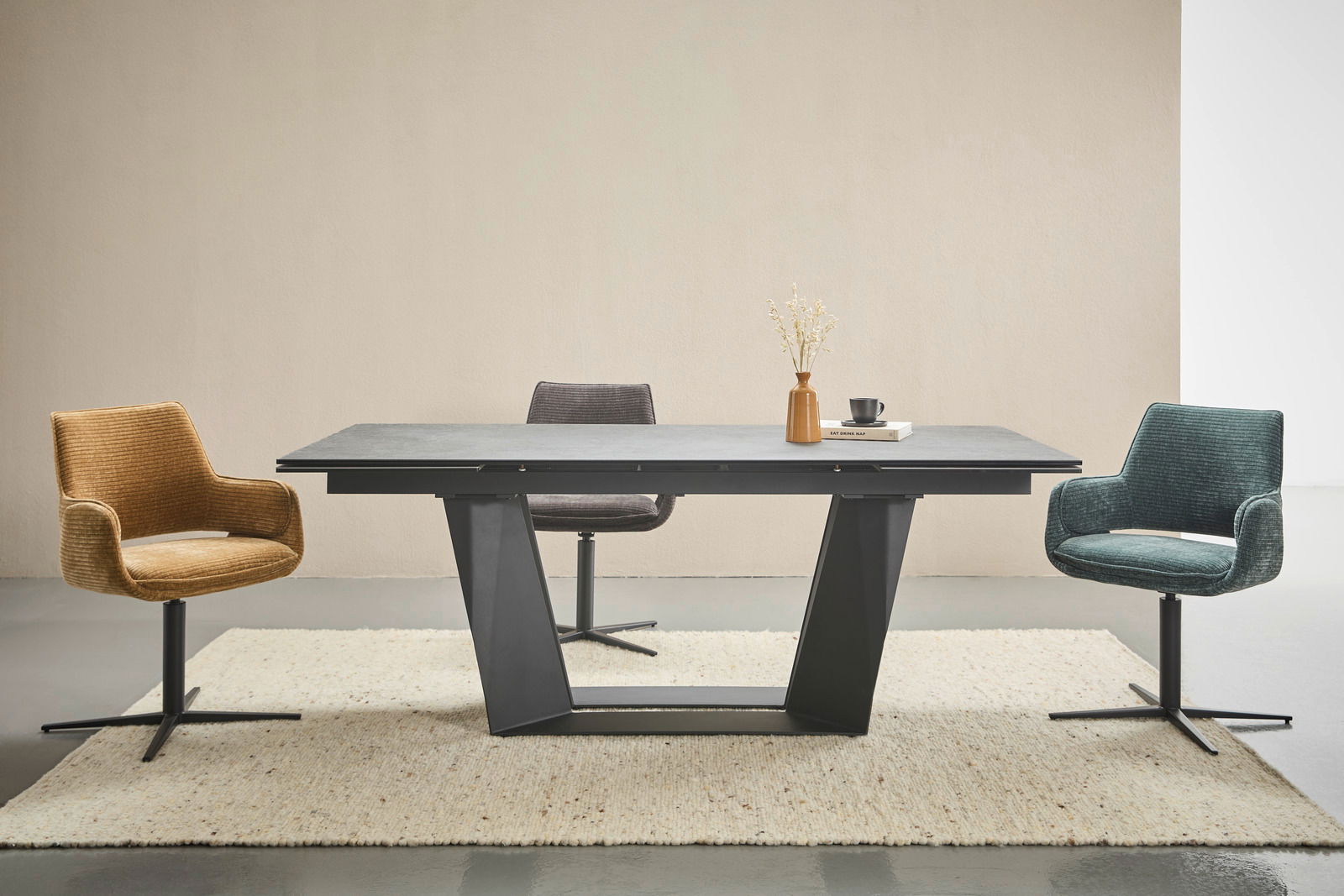 Moderner Esstisch mit schwarzem Gestell und grauer Tischplatte, umgeben von drei farbigen Stühlen in einem hellen Raum, Frontalansicht.