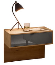 Moderner Nachtschrank aus Holz mit einer Schublade in dunklem Glas, darauf eine stilvolle Lampe und ein Glas Wasser, seitliche Perspektive.
