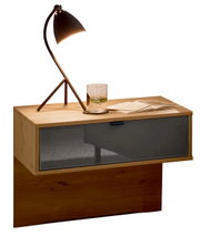 Modern houten nachtkastje met een lade van donker glas, met daarop een stijlvolle lamp en een glas water, gezien vanuit de zijkant.