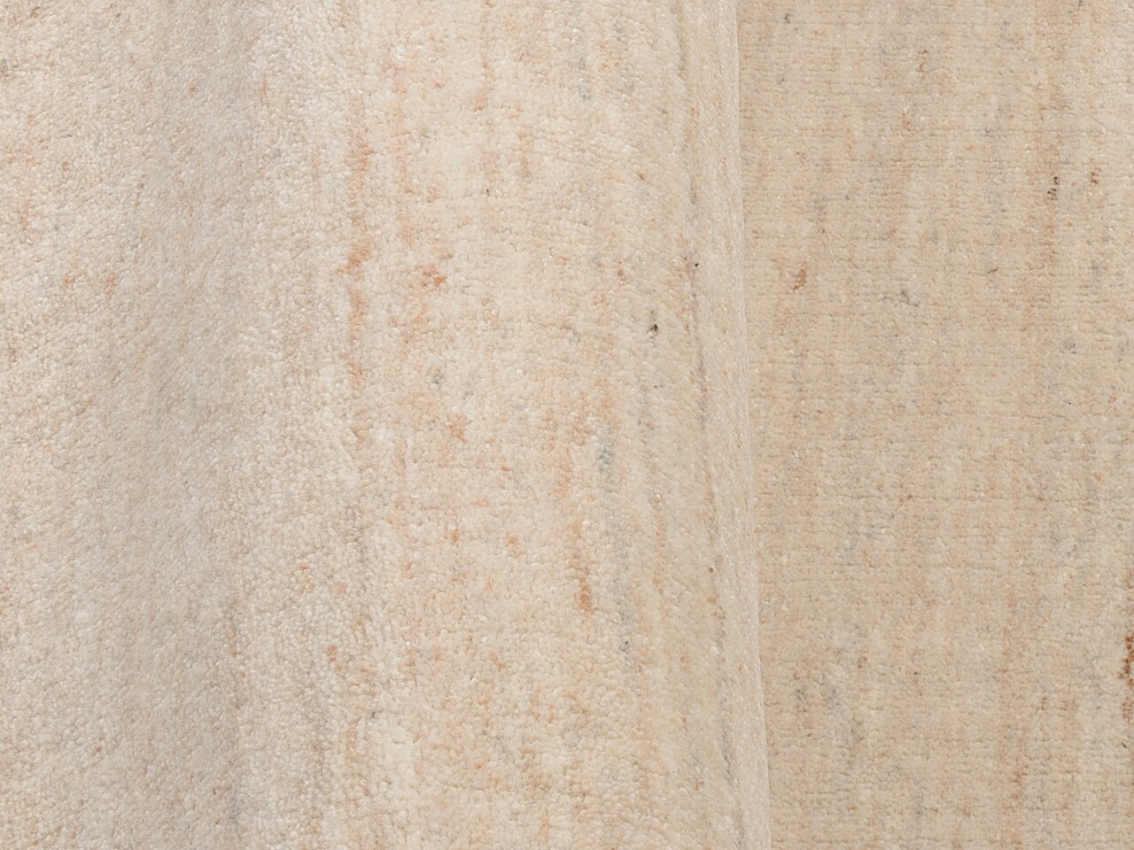Nahaufnahme eines beigen Wollteppichs mit dezenter Textur und leichtem Farbverlauf, seitliche Perspektive.