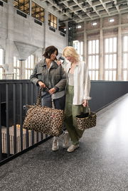 Zwei Frauen stehen in einem modernen Gebäude und tragen Taschen mit Leopardenmuster. Die Perspektive zeigt die Taschen von vorne.