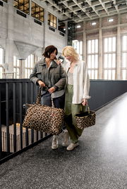 Zwei Frauen stehen in einem modernen Gebäude und tragen Taschen mit Leopardenmuster. Die Perspektive zeigt die Taschen von vorne.