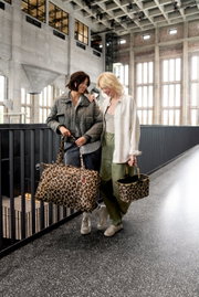 Zwei Frauen stehen in einem modernen Gebäude und tragen Taschen mit Leopardenmuster. Die Perspektive zeigt die Taschen von vorne.