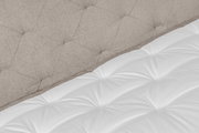 Nahaufnahme eines Boxspringbetts mit gepolstertem Kopfteil in Beige und weißer Matratze, seitliche Perspektive