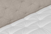 Nahaufnahme eines Boxspringbetts mit gepolstertem Kopfteil in Beige und weißer Matratze, seitliche Perspektive