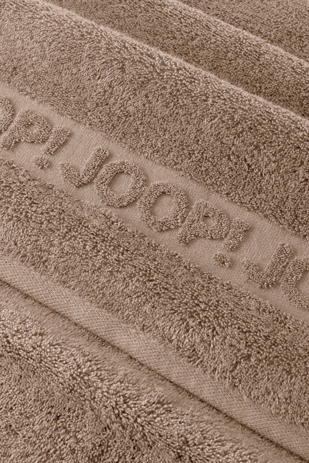 JOOP! Frottierset 5-teilig STUDIO Makro-Nahaufnahme aus schräger Draufsicht eines taupefarbenen Frottee-Handtuchs mit eingewebtem Schriftzug „JOOP!“ und weicher, strukturierter Oberfläche