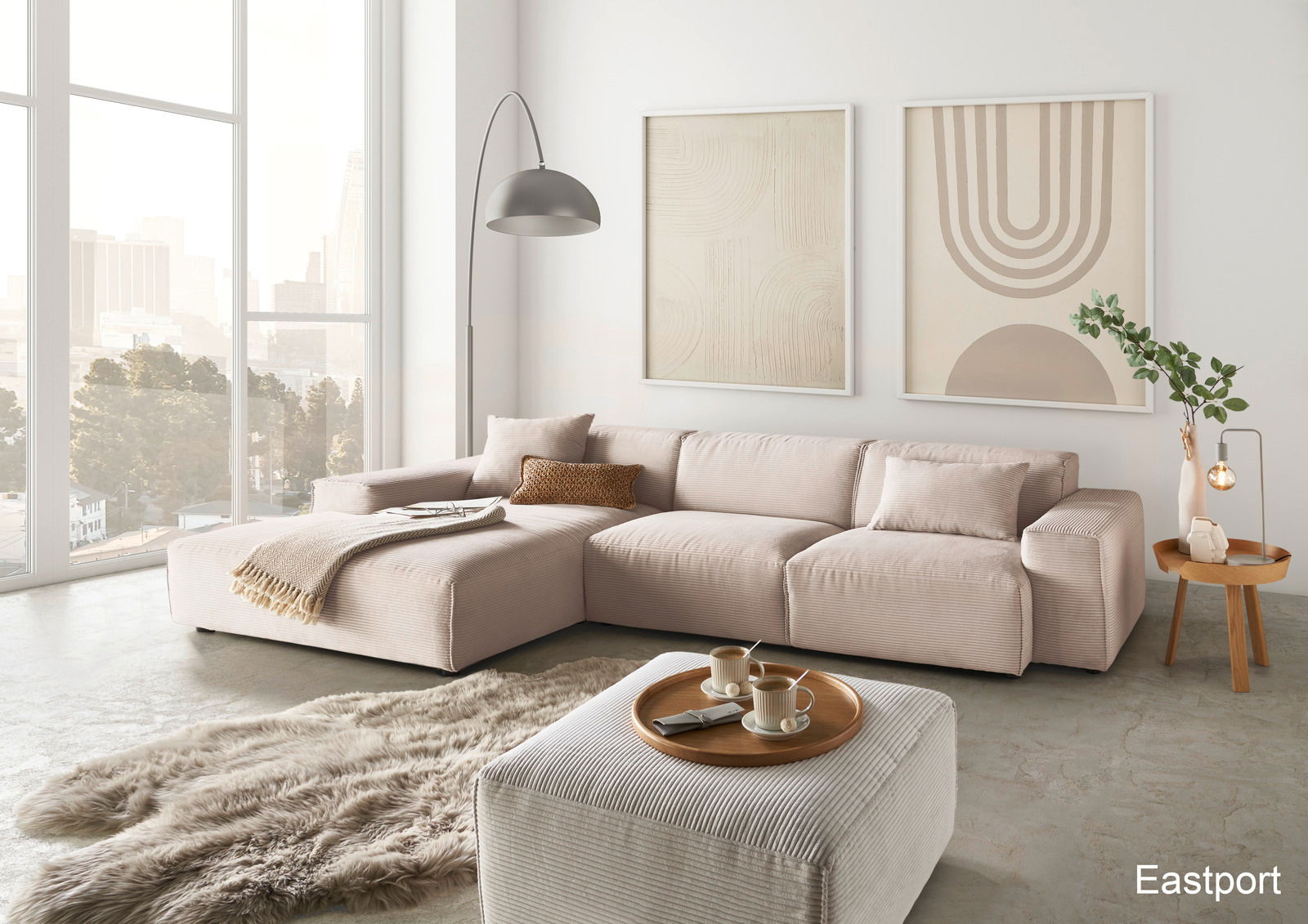 Lounge Handmade Ecksofa LH-EDINA Moderne Wohnzimmeransicht mit einer großen, beigen Eckcouch in einem hellen Raum mit großen Fenstern, einem flauschigen Teppich und stilvollen Wandbildern.