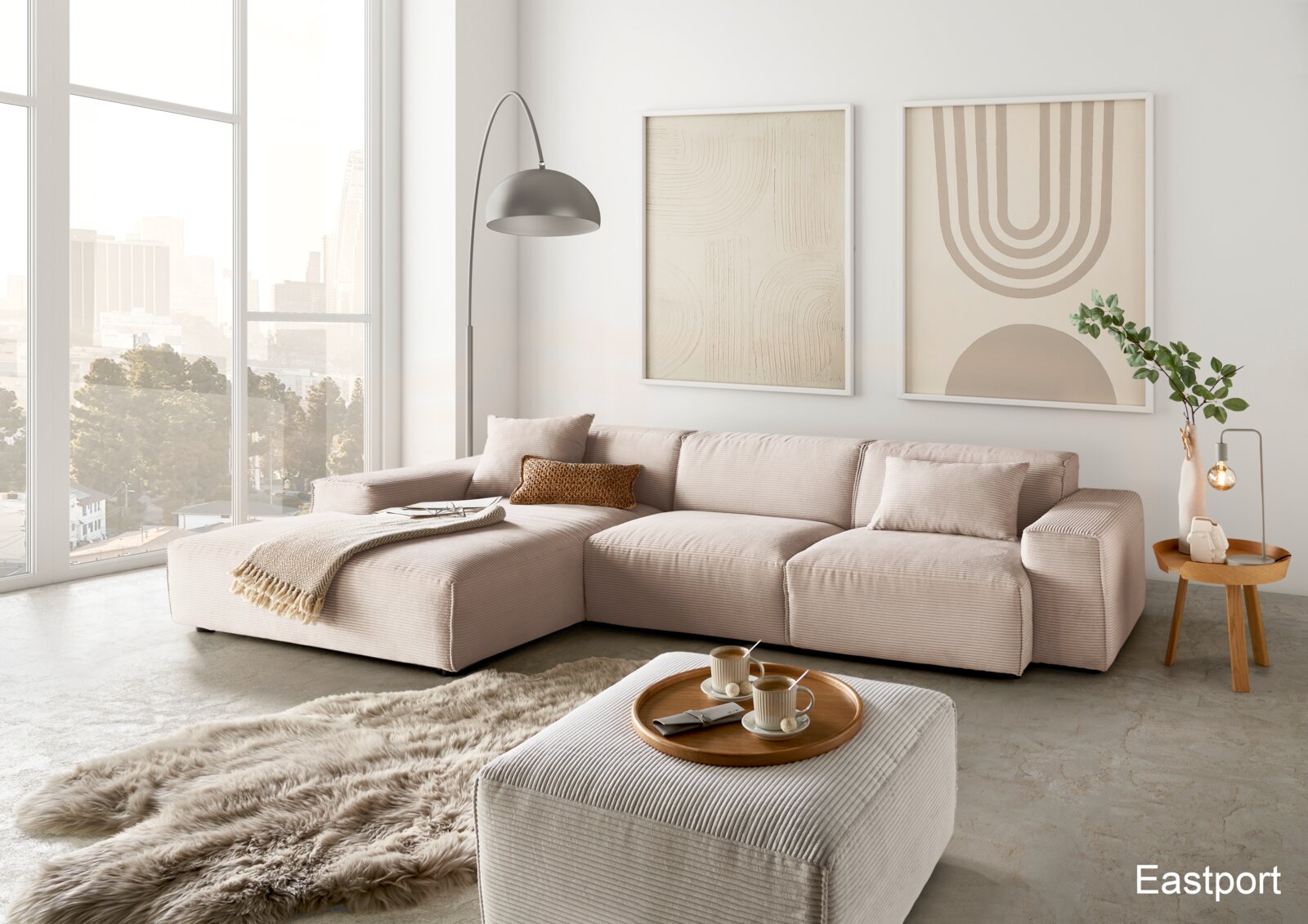 Moderne Wohnzimmeransicht mit einer großen, beigen Eckcouch in einem hellen Raum mit großen Fenstern, einem flauschigen Teppich und stilvollen Wandbildern.