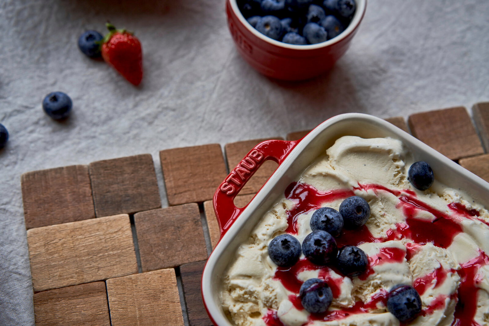 Rote Auflaufform mit Griffen, gefüllt mit Vanilleeis, Blaubeeren und roter Soße, aus der Vogelperspektive fotografiert.