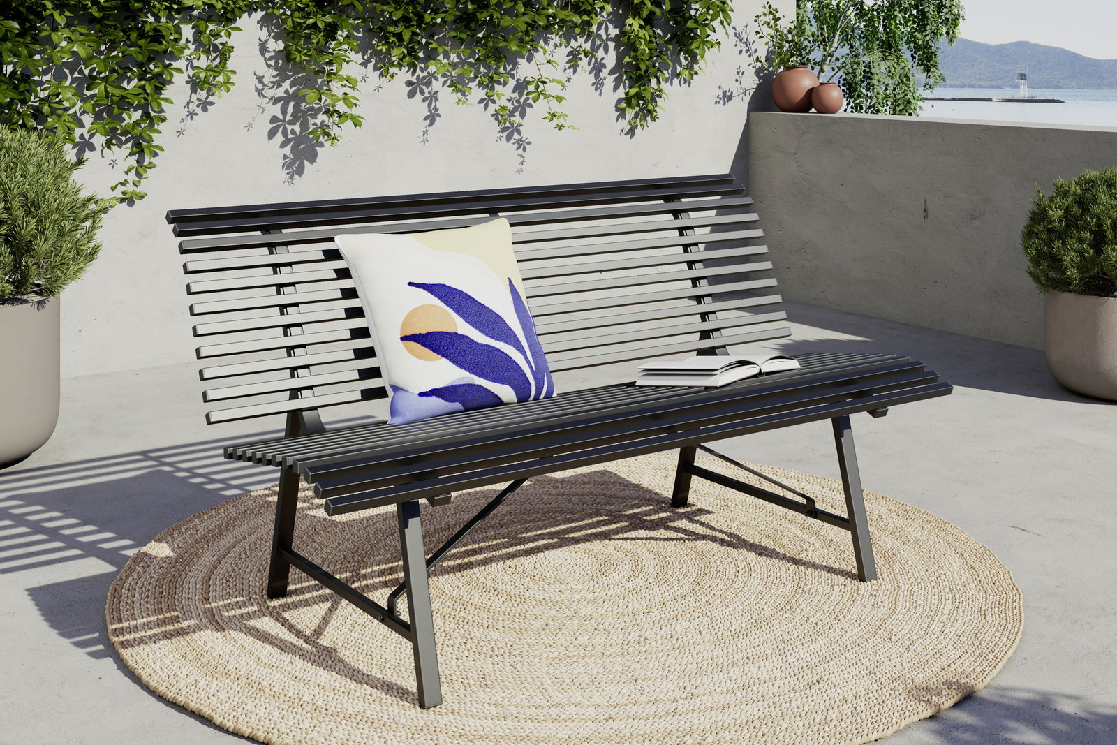 Ambia Garden Tuinbank ZWETL Moderne Gartenbank aus Metall mit Kissen und Buch, seitliche Perspektive, auf einer Terrasse mit Pflanzen im Hintergrund.