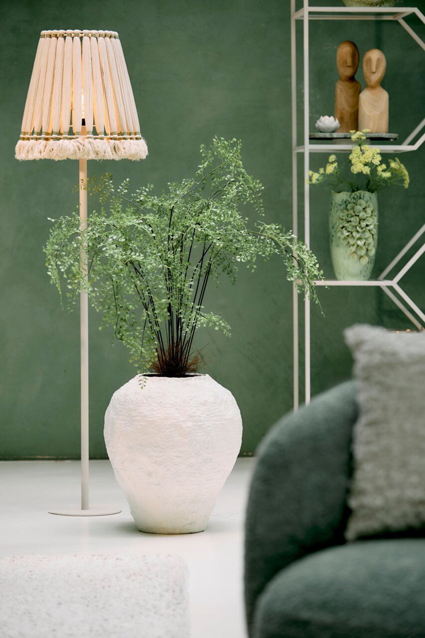 Staande lamp met een natuurlijke lampenkap van houten staafjes, op de achtergrond een groene ruimte met decoratieve elementen, zijaanzicht.