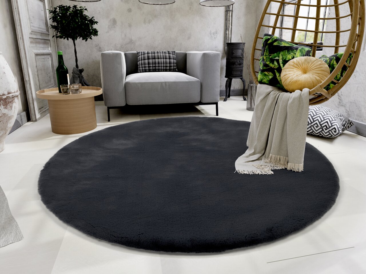 Runder, dunkelgrauer Fellteppich in einem modernen Wohnzimmer mit grauem Sofa, rundem Holztisch und hängendem Stuhl. Perspektive von oben.