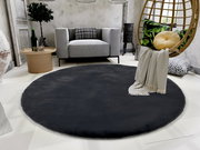 Runder, dunkelgrauer Fellteppich in einem modernen Wohnzimmer mit grauem Sofa, rundem Holztisch und hängendem Stuhl. Perspektive von oben.