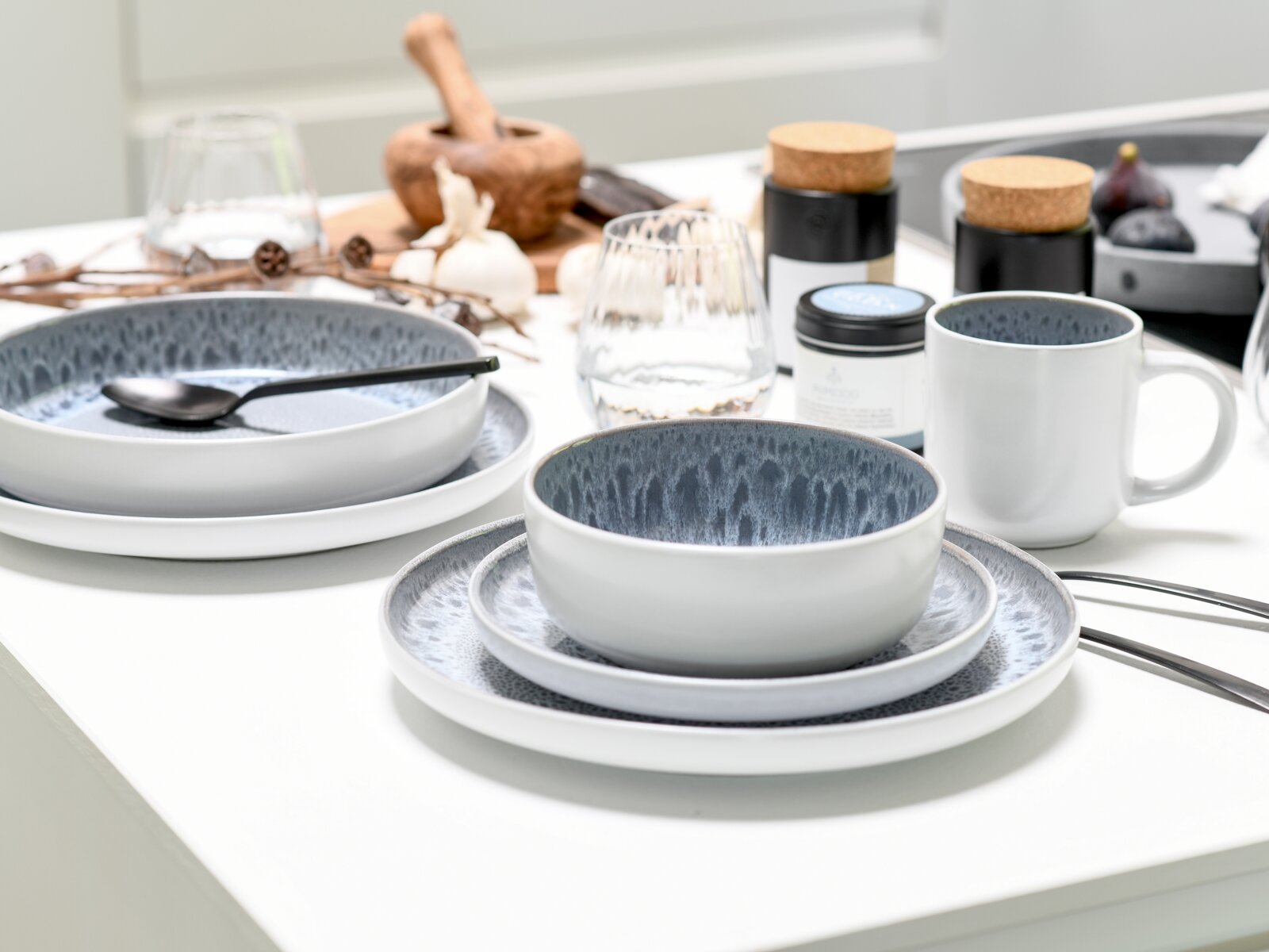 Kombiservice 16-tlg. Stone auf einem Tisch, bestehend aus Tellern, Schalen und einer Tasse in modernem Design mit grauem und weißem Farbverlauf, seitliche Perspektive.