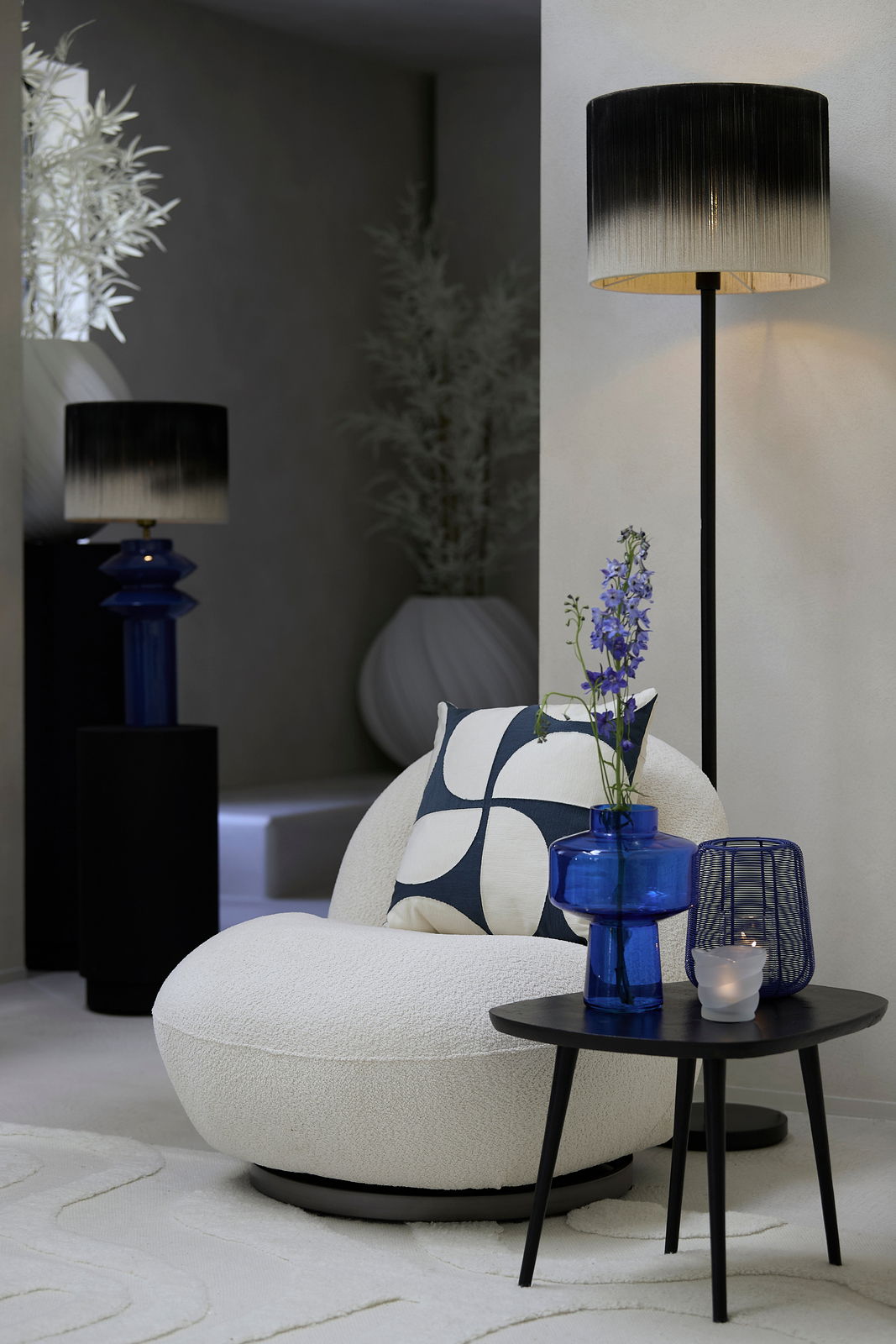 Moderne Stehleuchte mit schwarzem und weißem Farbverlauf, in einem stilvoll eingerichteten Raum mit einem Sessel und einem Beistelltisch, seitliche Perspektive.