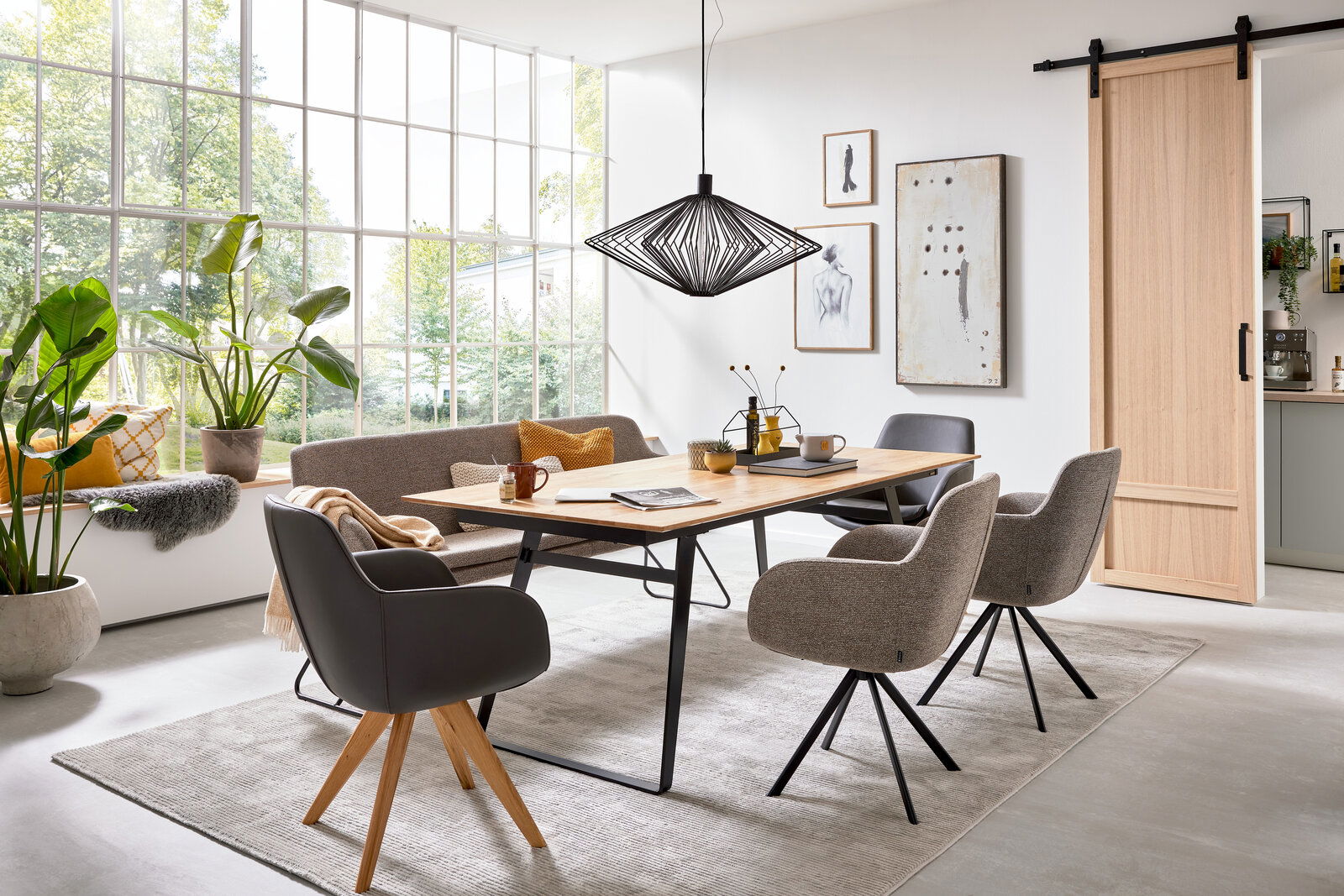 Esszimmer mit modernem Esstisch aus Holz und stilvollen Sesseln in einem hellen Raum mit großen Fenstern, seitliche Perspektive