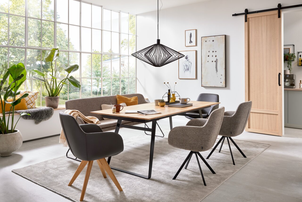 Esszimmer mit modernem Esstisch aus Holz und stilvollen Sesseln in einem hellen Raum mit großen Fenstern, seitliche Perspektive