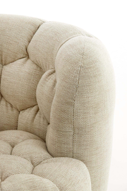 Detailansicht eines beigen Sessels mit gepolstertem Stoff und Knopfheftung.