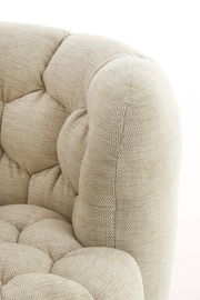 Detailansicht eines beigen Sessels mit gepolstertem Stoff und Knopfheftung.