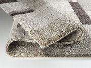 Nahaufnahme eines Hochflorteppichs Castle Beppo in Beige- und Brauntönen, teilweise aufgerollt, um die Textur und Dicke zu zeigen.