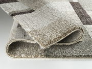 Nahaufnahme eines Hochflorteppichs Castle Beppo in Beige- und Brauntönen, teilweise aufgerollt, um die Textur und Dicke zu zeigen.