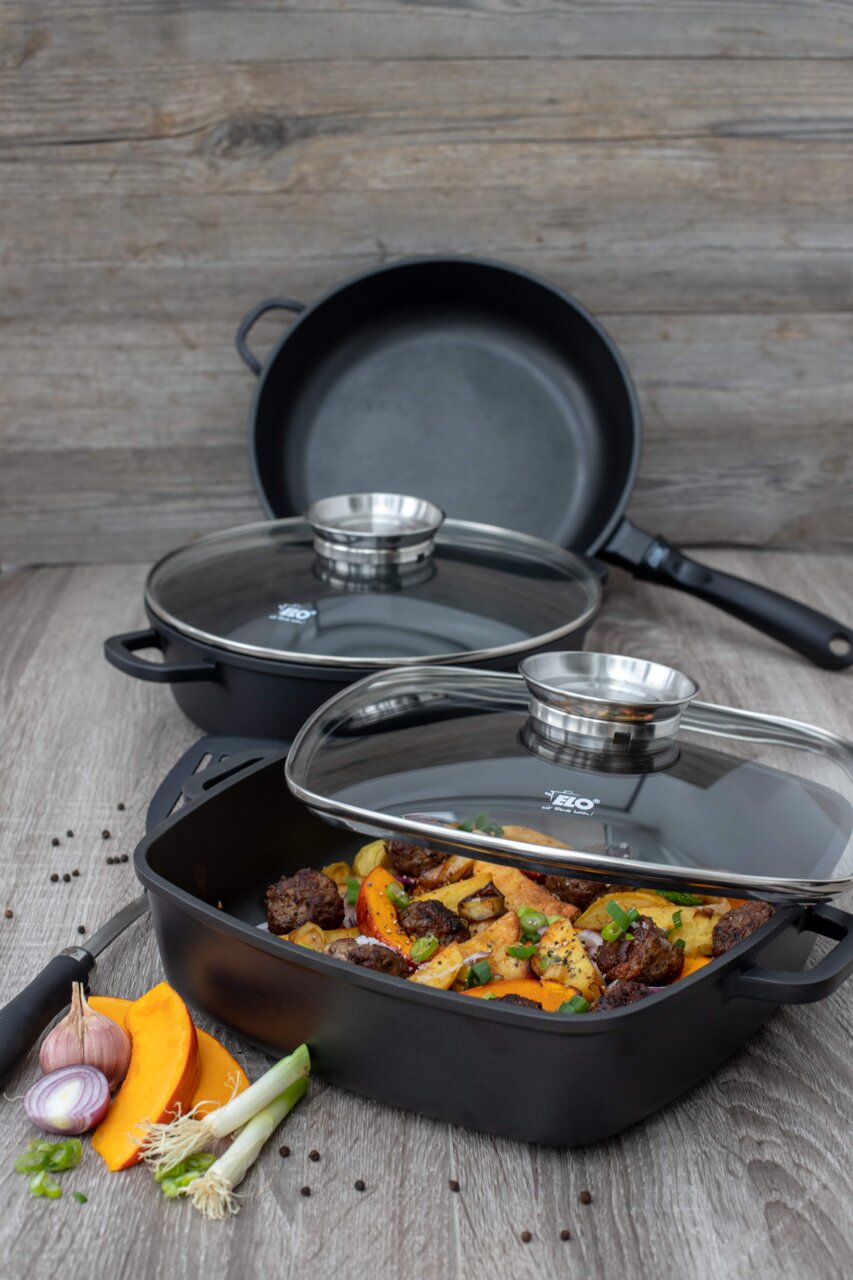 Alucast Servierpfanne rund 28 cm mit Glasdeckel, gefüllt mit gebratenem Gemüse und Fleisch, auf einem Holztisch aus der Seitenperspektive fotografiert.