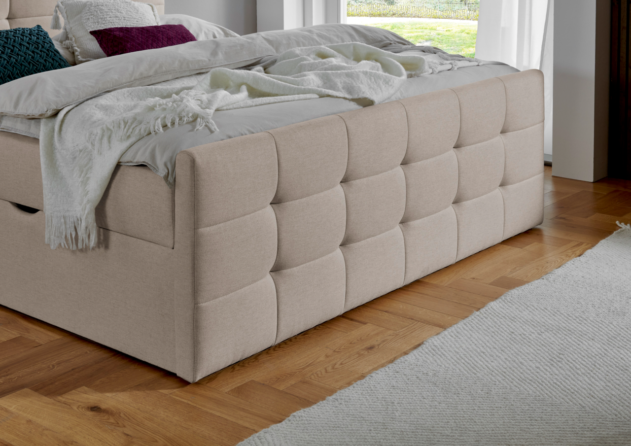 Beige Boxbett mit gestepptem Kopfteil, seitlicher Blick auf das Bett in einem modernen Schlafzimmer mit Holzboden.