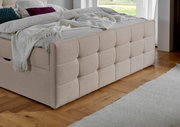 Beige Boxbett mit gestepptem Kopfteil, seitlicher Blick auf das Bett in einem modernen Schlafzimmer mit Holzboden.