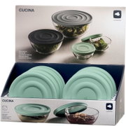 Silikondeckel in Salbeigrün, präsentiert in einer Verkaufsverpackung. Der Deckel ist auf einer Glasschüssel platziert, die mit Salat gefüllt ist. Perspektive von vorne.