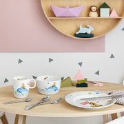Kinderbesteck-Set mit bunten Tiermotiven, bestehend aus Tasse, Schüssel, Teller und Besteck, auf einem Holztisch in einer verspielten Umgebung präsentiert. Perspektive: Frontalansicht.