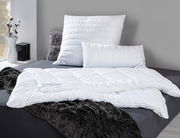 Faserdecke Duo ANTIGUA von billerbeck auf einem Bett, umgeben von Kissen und einer flauschigen Decke, seitliche Perspektive