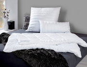 Faserdecke Duo ANTIGUA von billerbeck auf einem Bett, umgeben von Kissen und einer flauschigen Decke, seitliche Perspektive