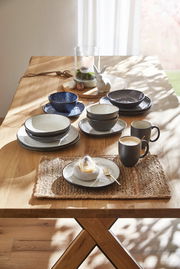 Ein stilvolles Kombiset aus grauem Geschirr, bestehend aus Tellern, Schalen und Tassen, auf einem Holztisch arrangiert. Die Perspektive zeigt das Set von oben in einem hellen Raum mit natürlichem Licht.