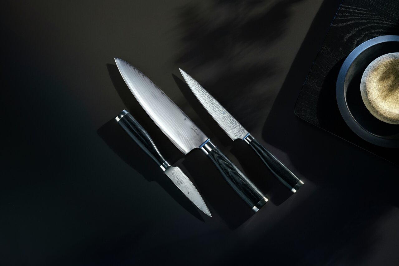 Dreiteiliges Messerset Yari aus der Vogelperspektive, bestehend aus einem großen Kochmesser, einem mittleren Allzweckmesser und einem kleinen Schälmesser, auf dunklem Hintergrund.