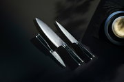 Dreiteiliges Messerset Yari aus der Vogelperspektive, bestehend aus einem großen Kochmesser, einem mittleren Allzweckmesser und einem kleinen Schälmesser, auf dunklem Hintergrund.