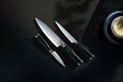 Dreiteiliges Messerset Yari aus der Vogelperspektive, bestehend aus einem großen Kochmesser, einem mittleren Allzweckmesser und einem kleinen Schälmesser, auf dunklem Hintergrund.