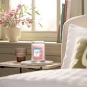 Yankee Candle Pink Sands Duftkerze im großen Glas mit zwei brennenden Dochten, frontal in einem sonnigen Wohnambiente präsentiert