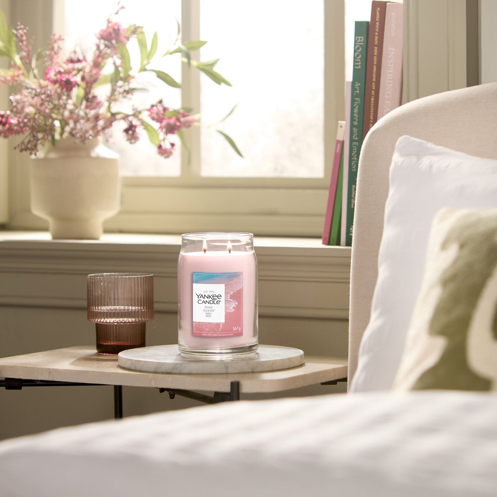 Yankee Candle Pink Sands Duftkerze im großen Glas mit zwei brennenden Dochten, frontal in einem sonnigen Wohnambiente präsentiert