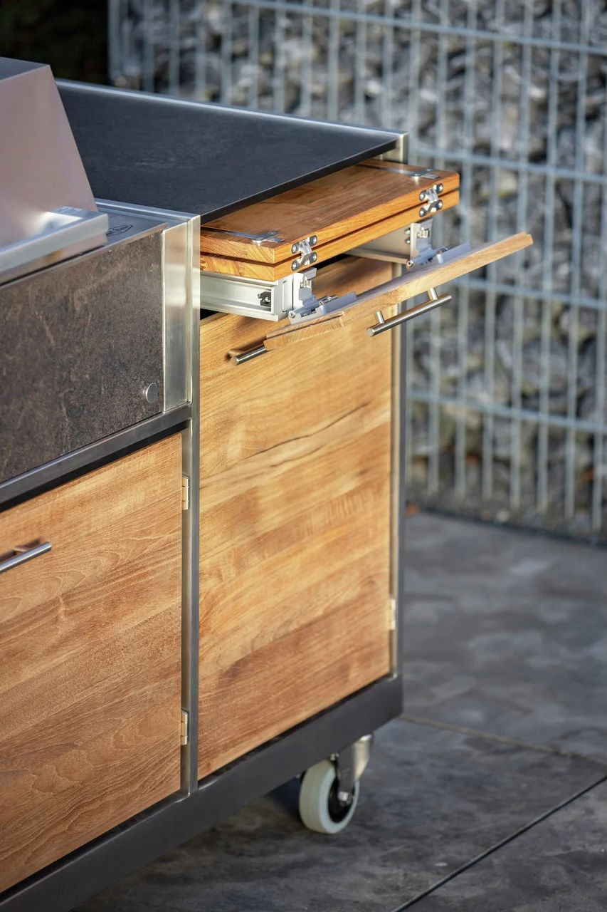 Nahaufnahme einer modernen Küchenzeile für den Außenbereich mit Metall- und Holzelementen, die mit einer Schublade und Rädern für Mobilität ausgestattet ist.