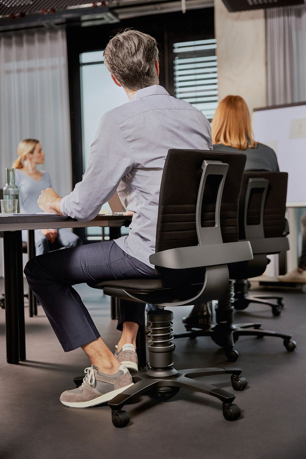 Rückansicht eines modernen Drehstuhls in einem Büro, mit Personen, die an einem Tisch sitzen.