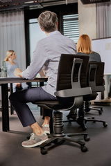 Rückansicht eines modernen Drehstuhls in einem Büro, mit Personen, die an einem Tisch sitzen.