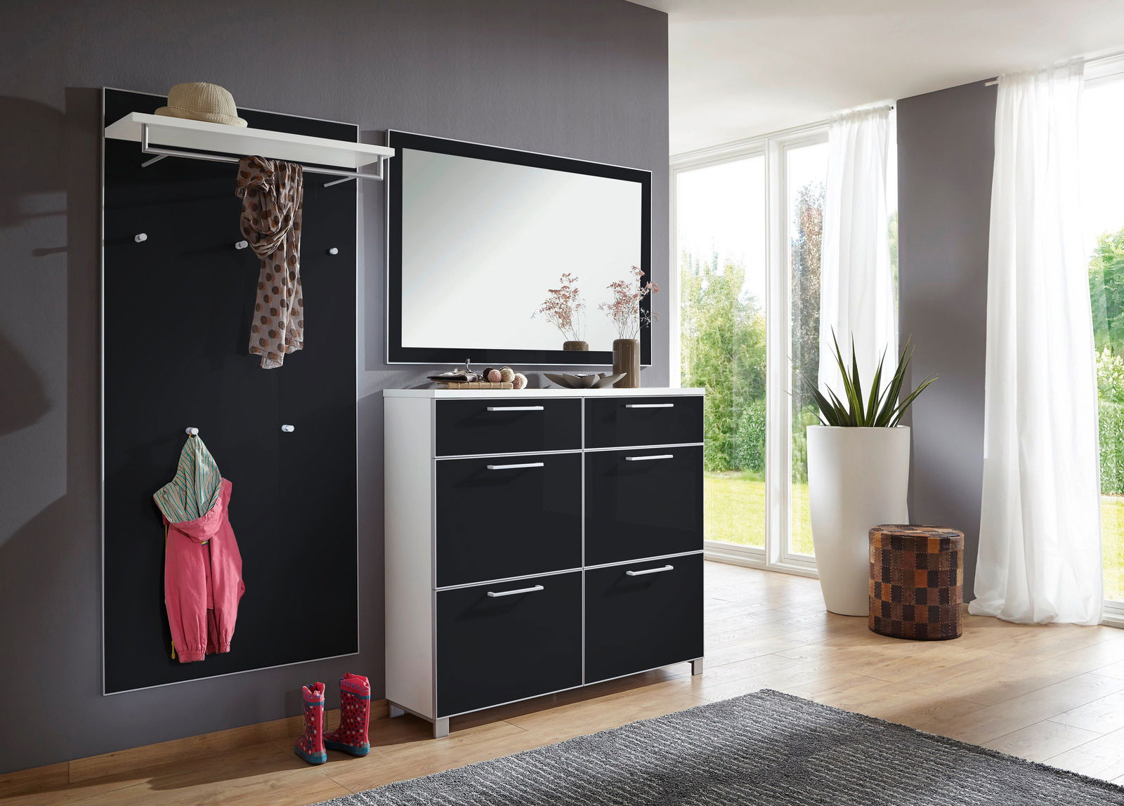 VOSS Garderoben-Set 3-tlg. SANTINA Modernes Garderoben-Set in einem hellen Raum mit großem Fenster, bestehend aus einer schwarzen Wandpaneele mit Haken, einem weißen Regalbrett und einem schwarzen Schuhschrank mit Spiegel. Perspektive von vorne.