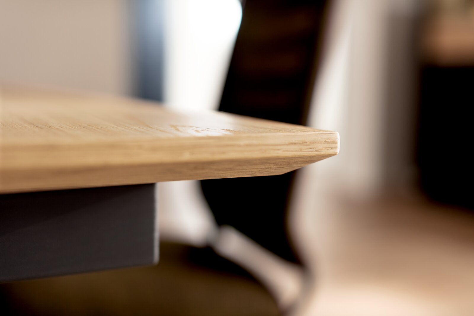Detailaufnahme aus seitlicher Perspektive: abgerundete Kante einer hellen Holz-Tischplatte mit sichtbarer Maserung, Hintergrund unscharf