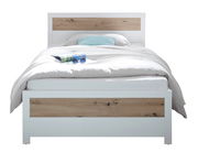 Modernes Bett mit weißem Rahmen und Holzakzenten, frontal fotografiert. Auf dem Bett liegt eine Zeitschrift und eine Sonnenbrille.