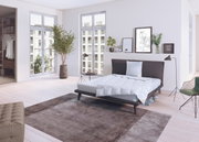 Moderne slaapkamer met een stijlvol bed, ingericht met een wit Spessarttraum CLASSIC-bed voor alle seizoenen en een driekamerkussen. Het perspectief toont het bed vanaf de zijkant in een lichte, elegante ruimte met grote ramen en een minimalistische inric